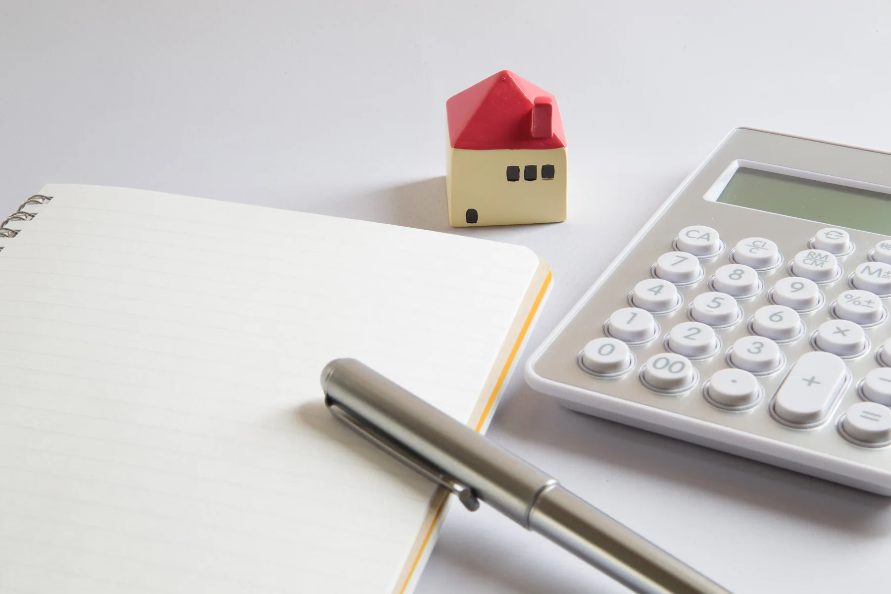Cuaderno, calculadora y una pequeña casa sobre una mesa.